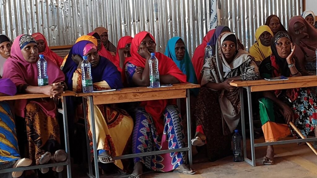 A group of women sit together at desks during a community training session in a Wa-PYDO project area.