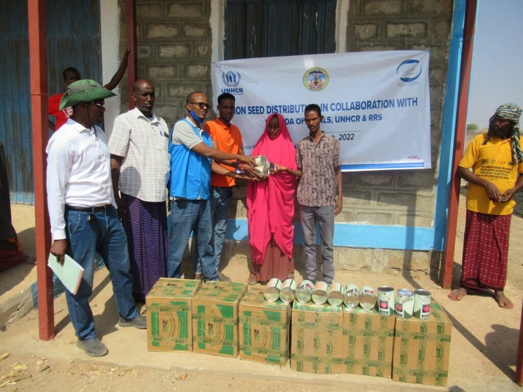 Seed distribution ceremony with UNHCR and RRS officials handing over onion seeds to a beneficiary as part of the livelihoods programme.